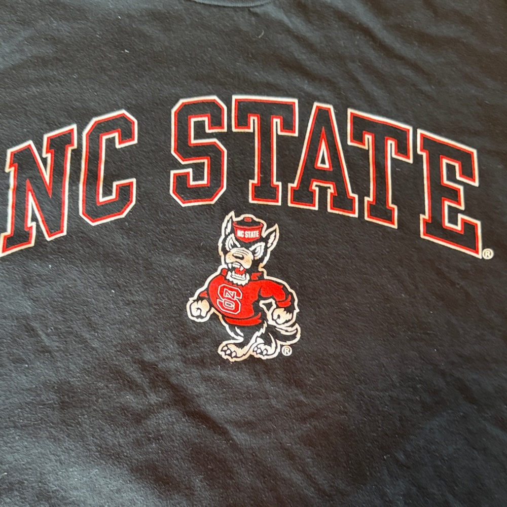 MV Sport brand Black NC State Tee. Adult MEDIUM. Sm tear at bottom.